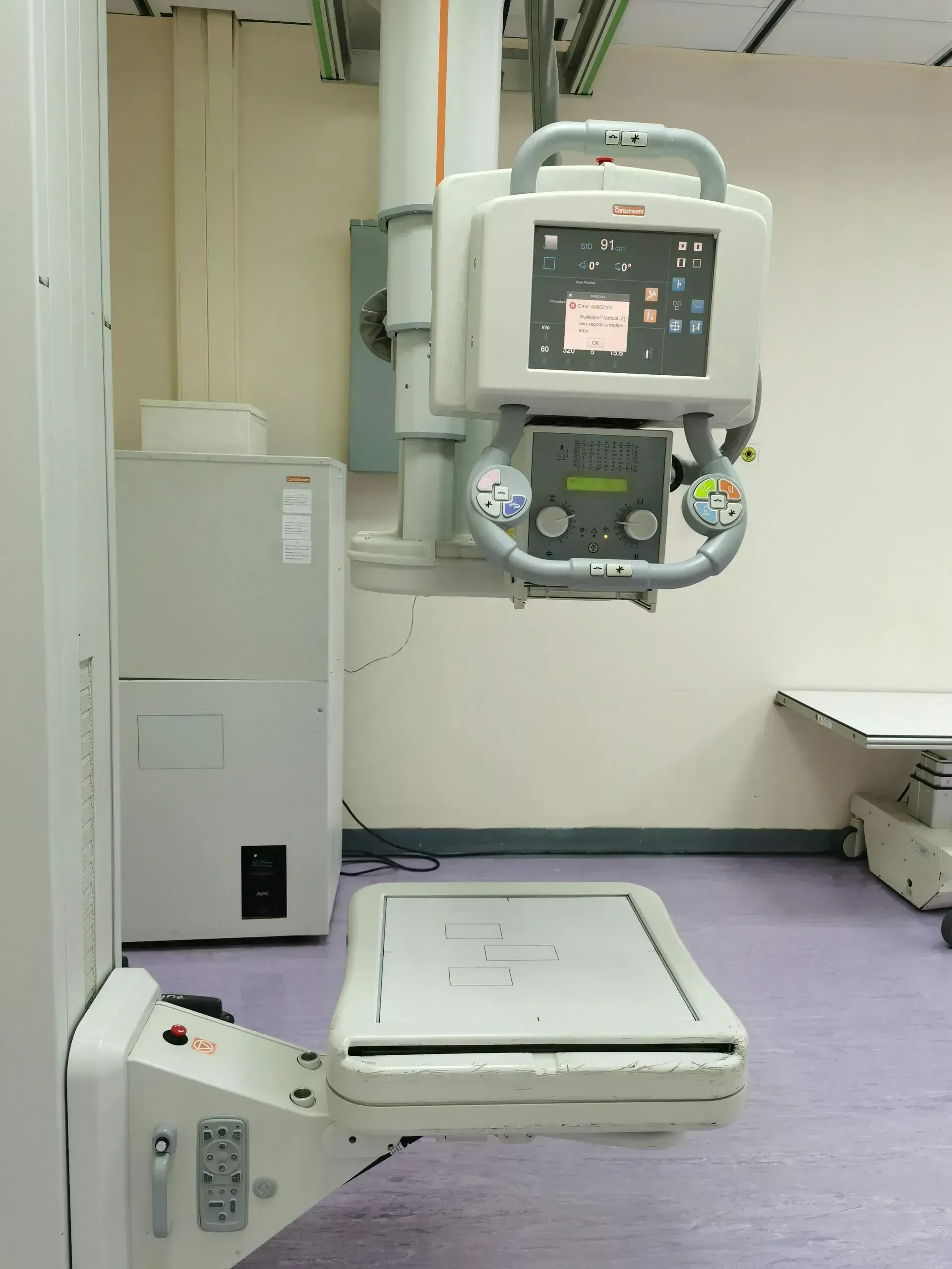 An X-ray machine with a digital display and examination platform in a medical imaging room.