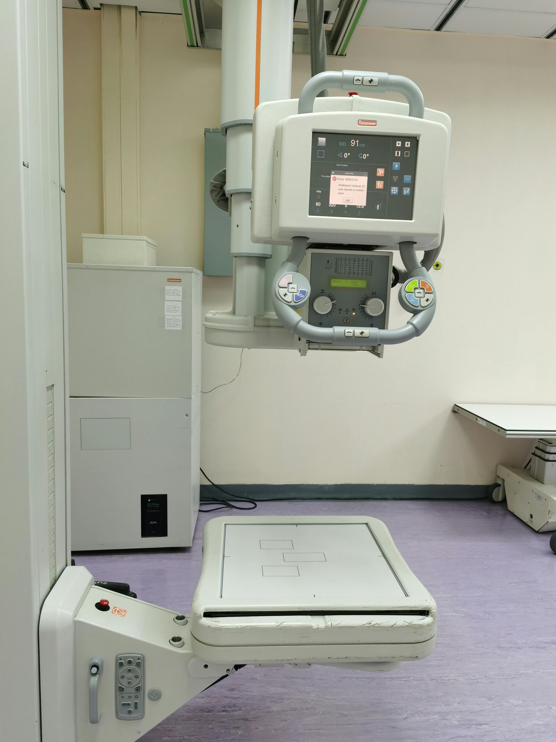 An X-ray machine with a digital display and examination platform in a medical imaging room.