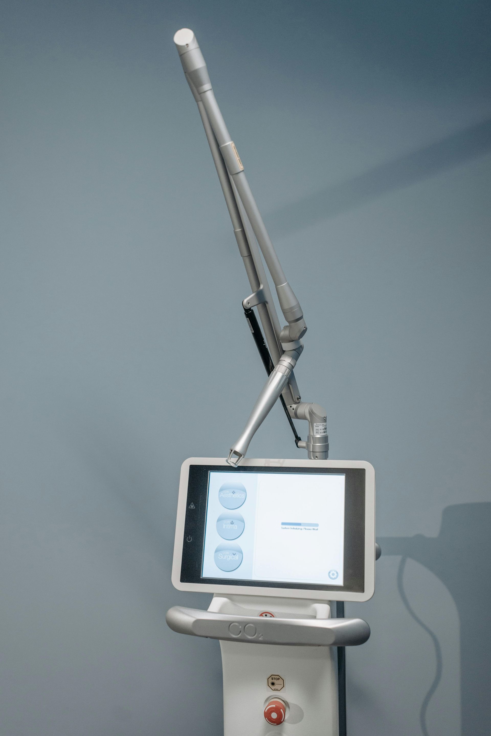 A medical laser device with an articulated arm and a digital touchscreen display against a plain wall.