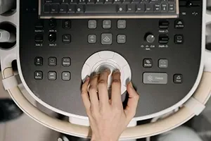 A hand operates the trackball control panel of an ultrasound machine.