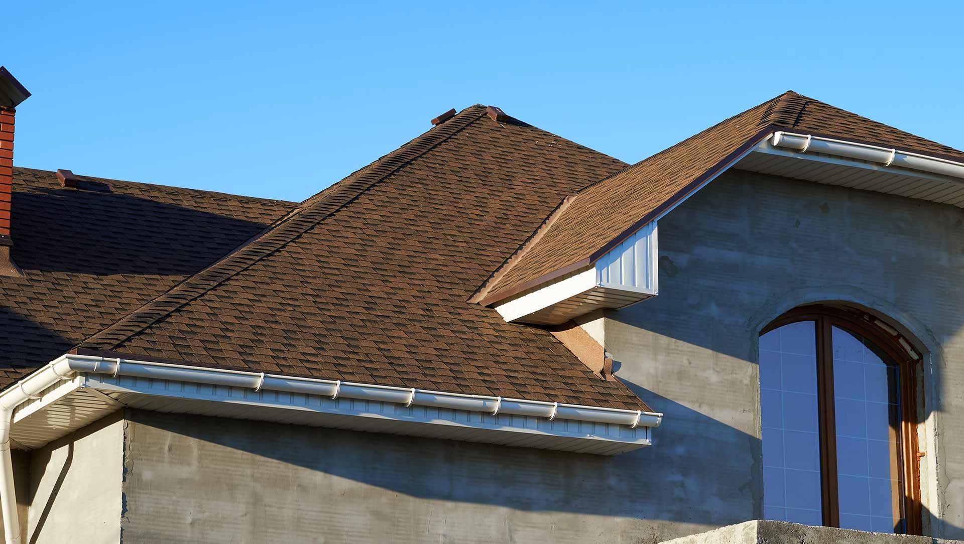 Brown shingled roof and blue stucco house exterior with arched window under clear sky