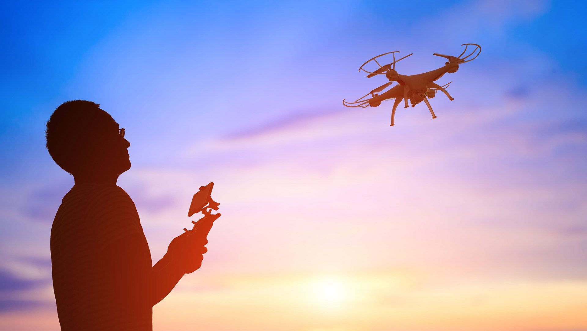 Silhouette of a person flying a drone against a colorful sunset sky