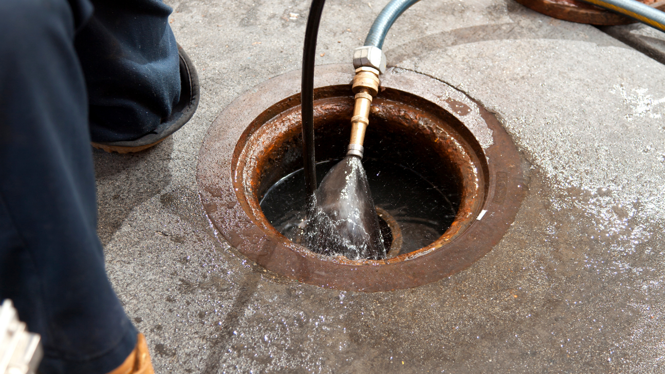 A hose spraying water into a circular drain hole in a concrete surface.
