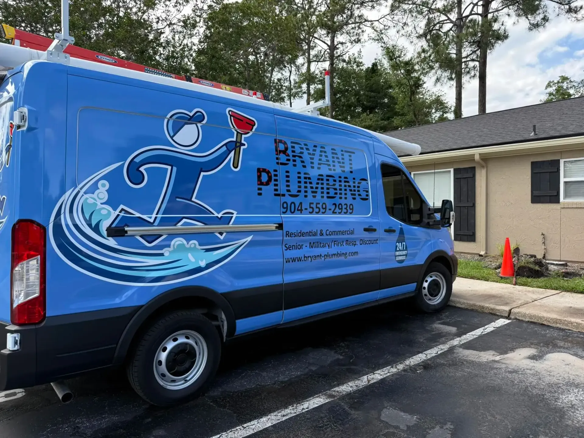 Blue plumbing service van parked outside a building, with a large plumber logo on the side.