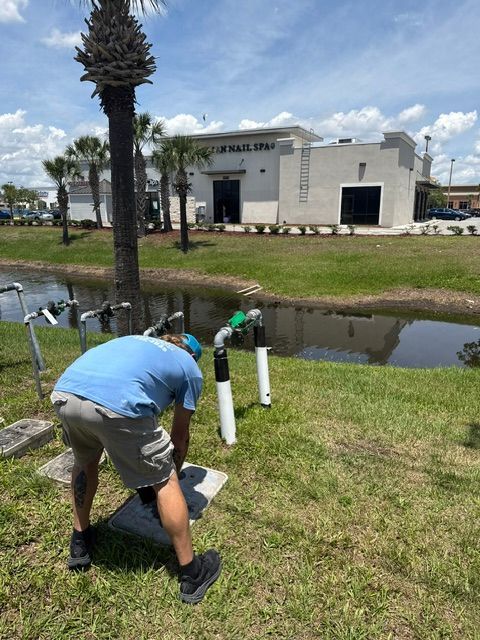 Two workers inspect white pipes beside a canal near an industrial building on a sunny day