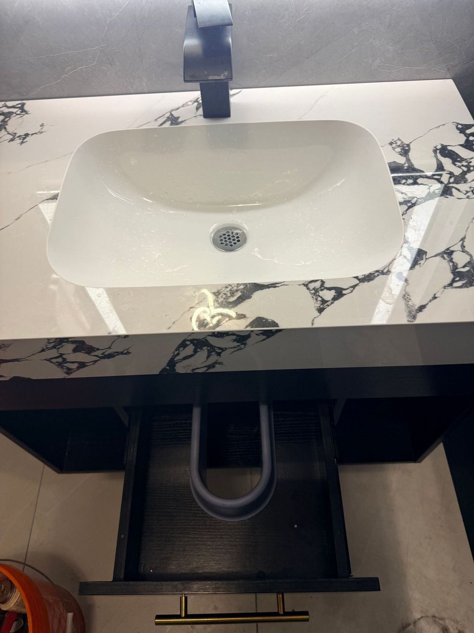 Modern bathroom sink with black faucet and marble countertop, showing plumbing below.