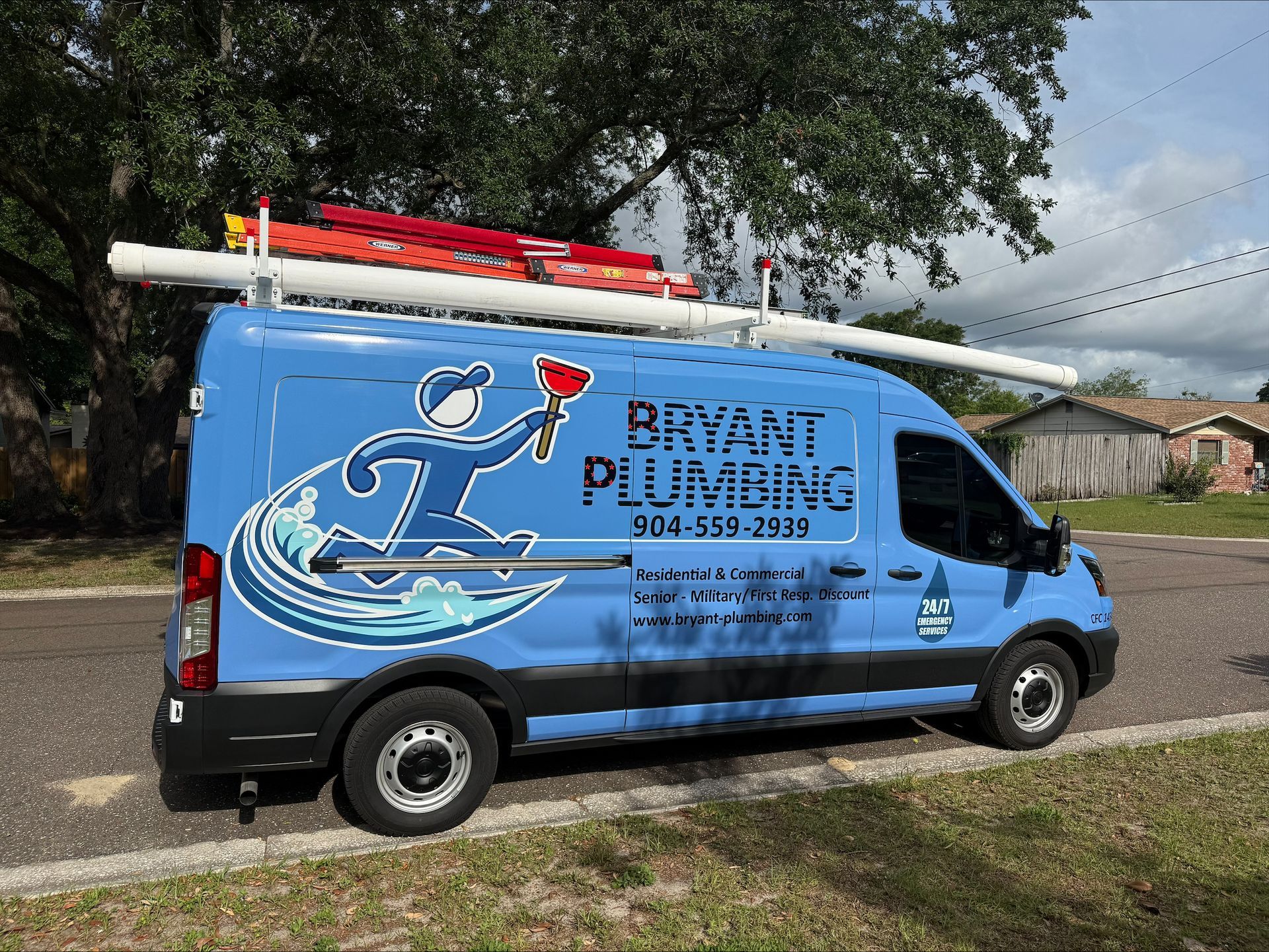 Blue plumbing service van parked on a gravel road under trees, with ladders on the roof.