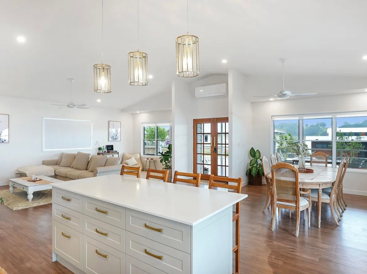 Open-concept Living Space With White Kitchen Island, Dining Area, And Living Room; Hardwood Floors, Light Colours — JGD Constructions in Lake Eacham, QLD