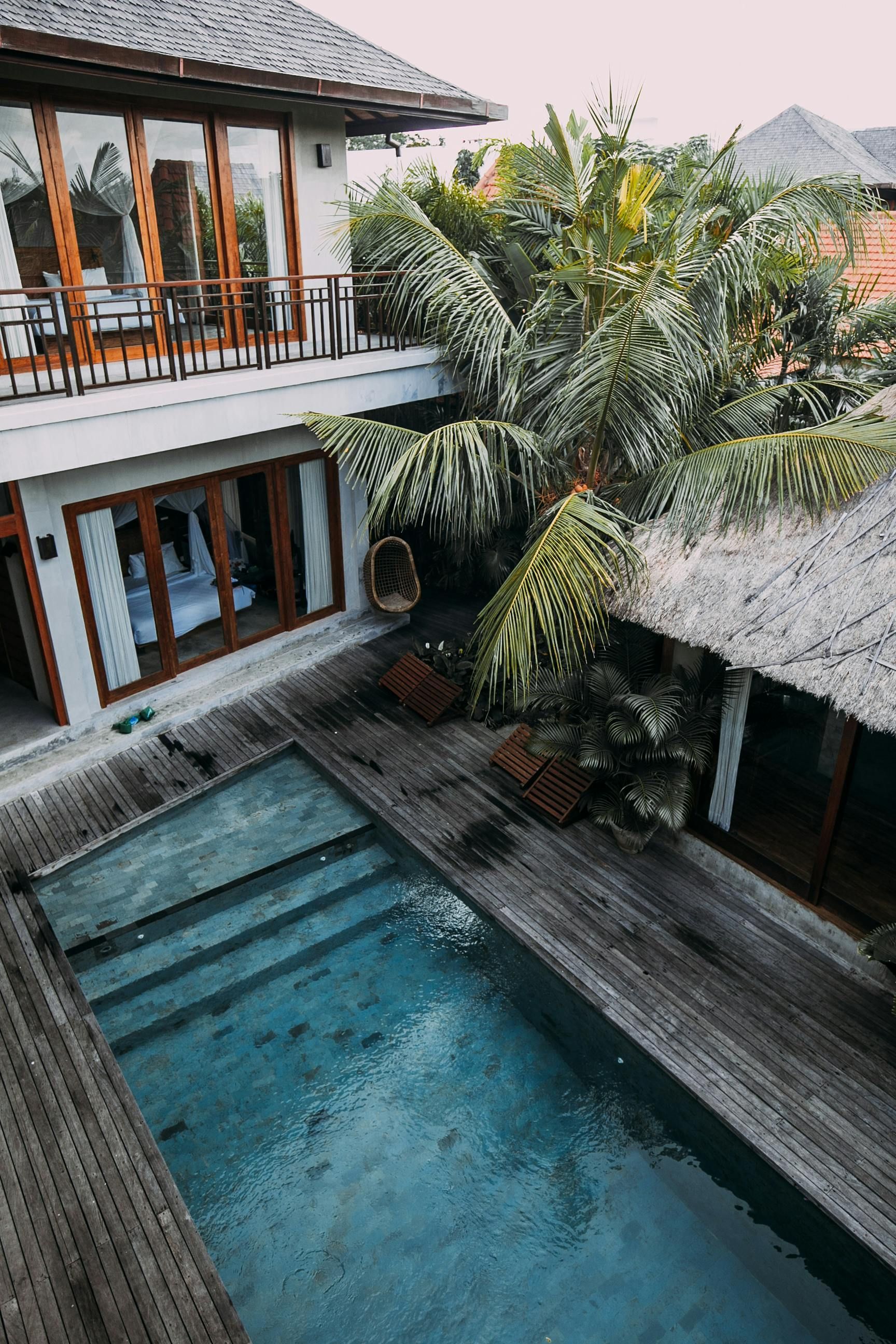 Two-story house with a pool, wooden deck, and lush greenery.