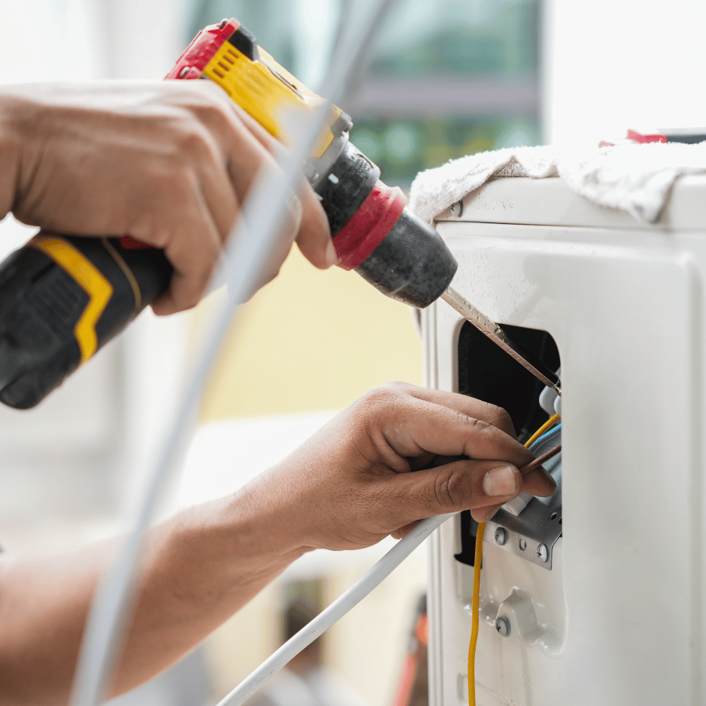 Hands drilling into an electrical box, wires visible, next to a white appliance.