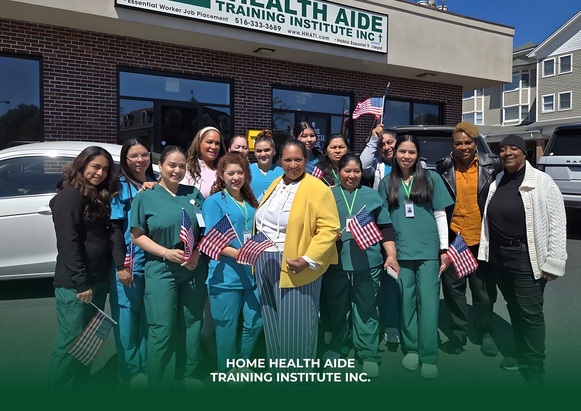 A group of students and staff in scrubs and casual clothing pose with small American flags outside a training institute.