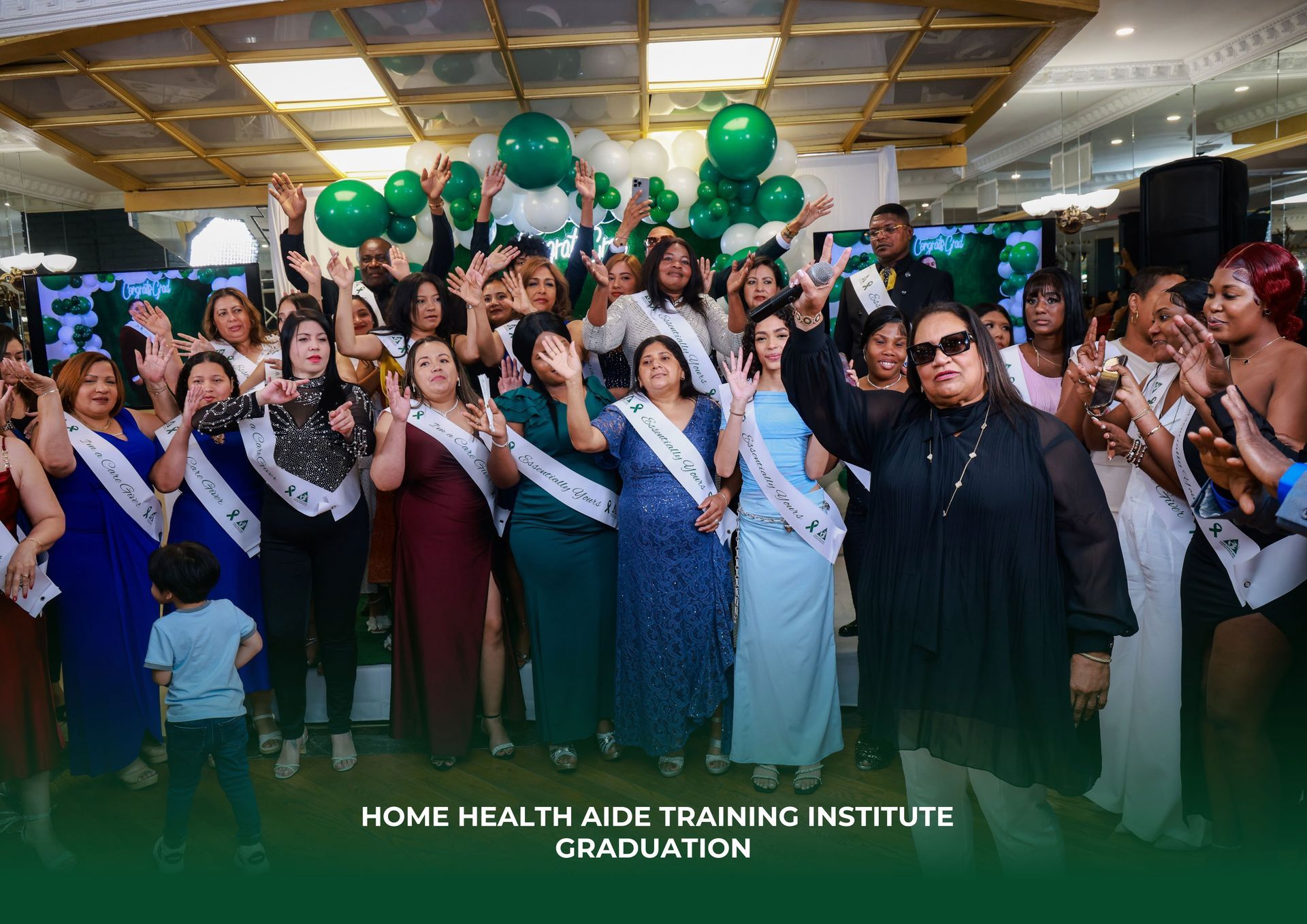 A graduation ceremony for a home health aide training institute with a group of people wearing sashes celebrating.