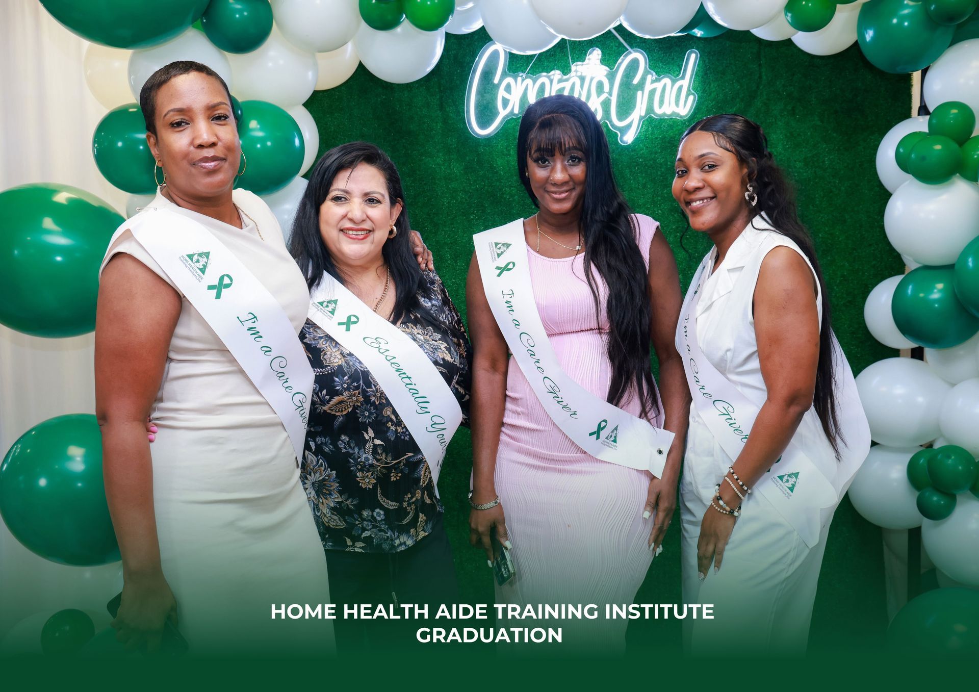 Four graduates wearing sashes stand before a green backdrop with balloons at a Home Health Aide Training Institute event.