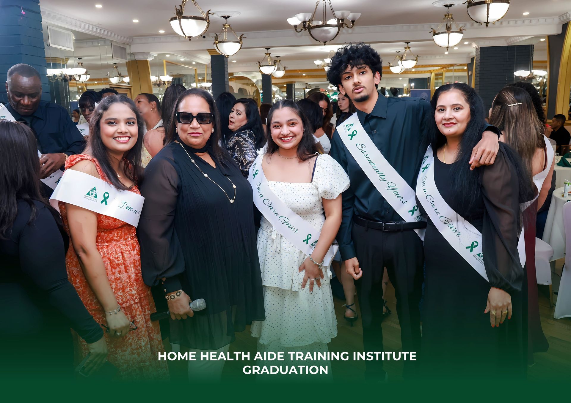 Five graduates in sashes stand together in a ballroom at a Home Health Aide Training Institute graduation.