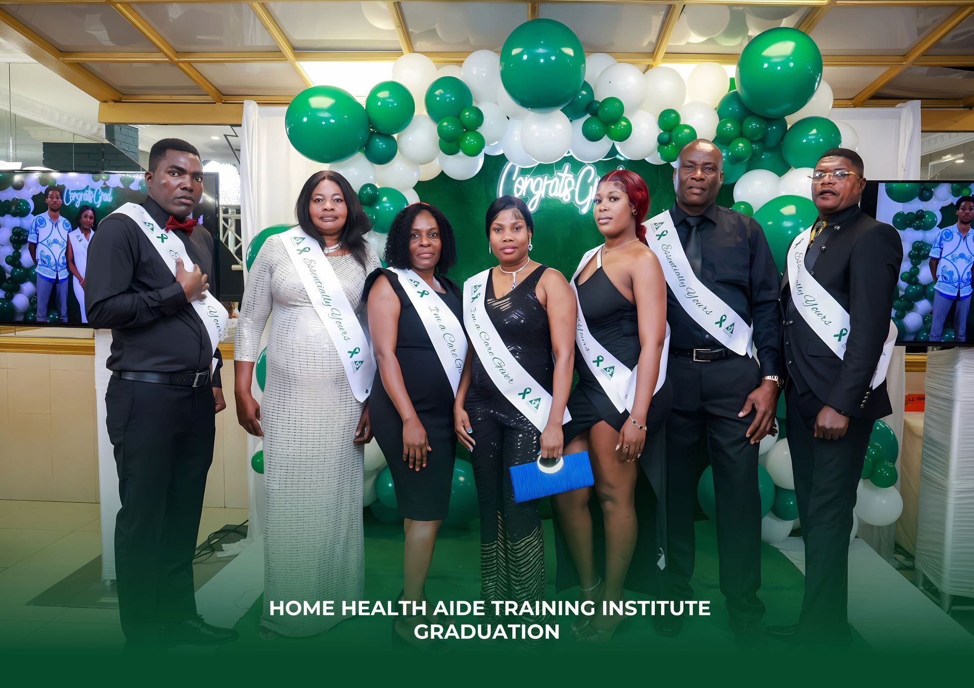 Graduates in formal attire pose in front of a green and white balloon arch at a Home Health Aide Training Institute event.