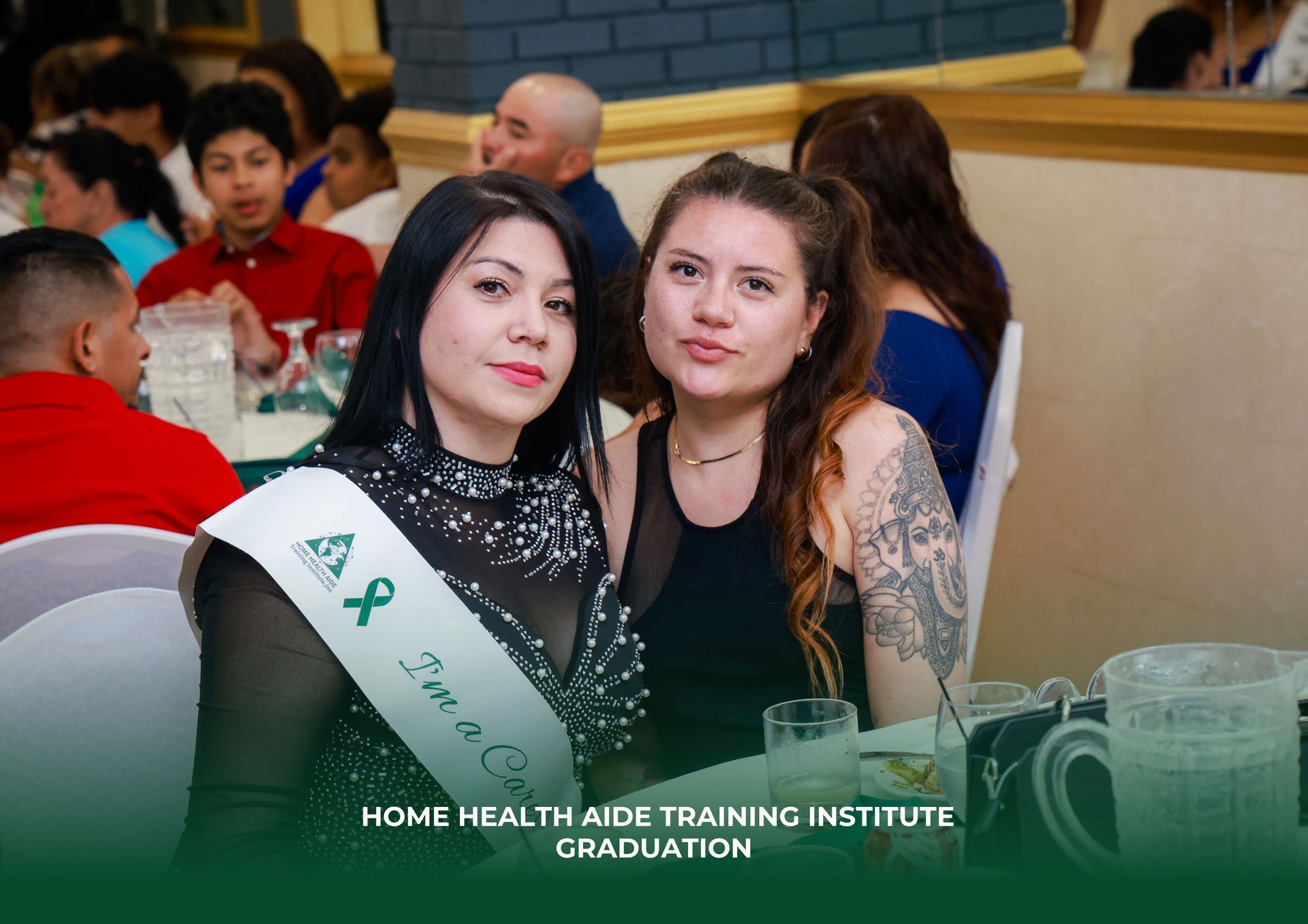 Two people at a Home Health Aide Training Institute graduation, wearing celebratory attire, sitting at a table together.