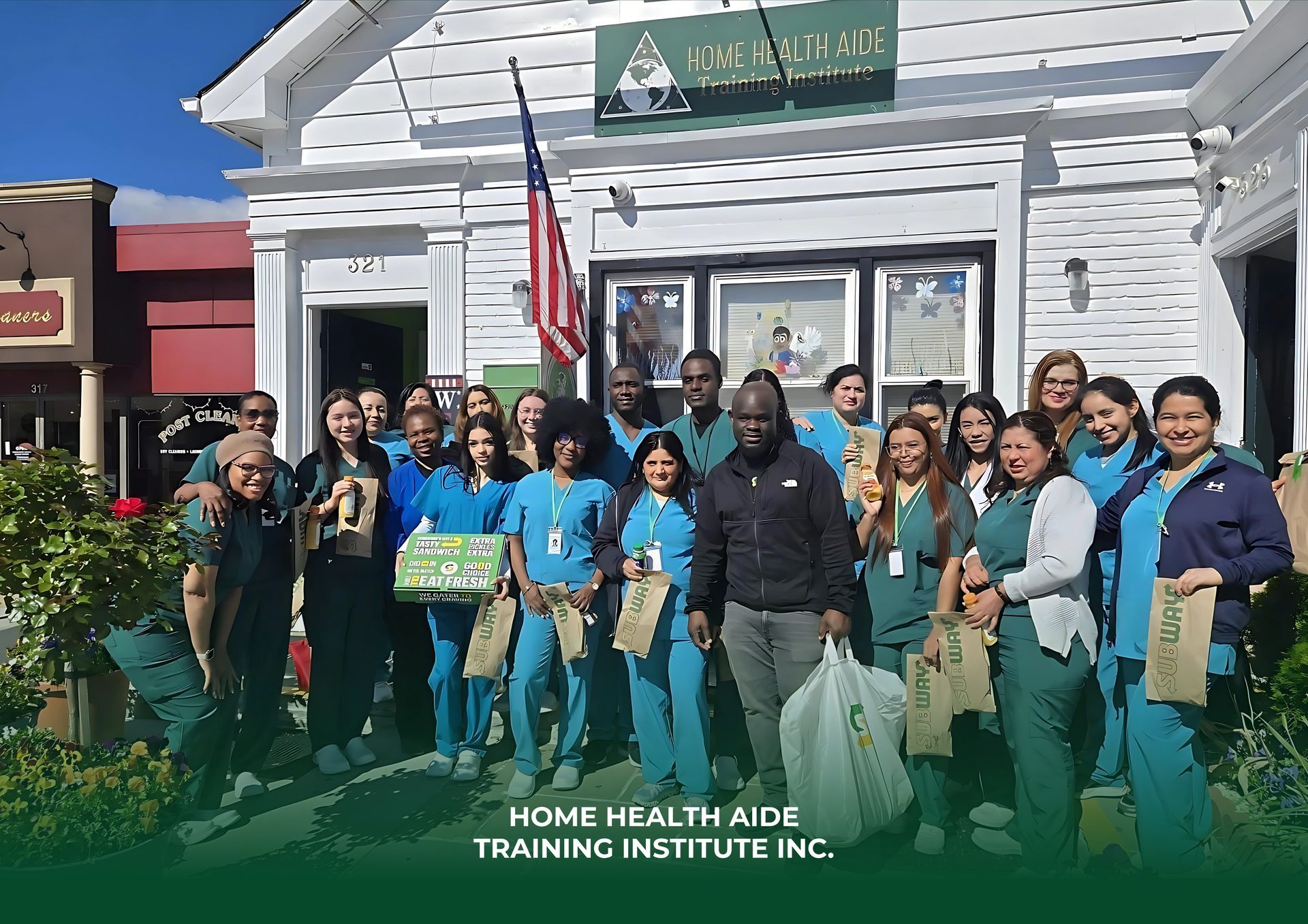 A large group of students in blue scrubs stands outside the Home Health Aide Training Institute Inc. holding gift bags.