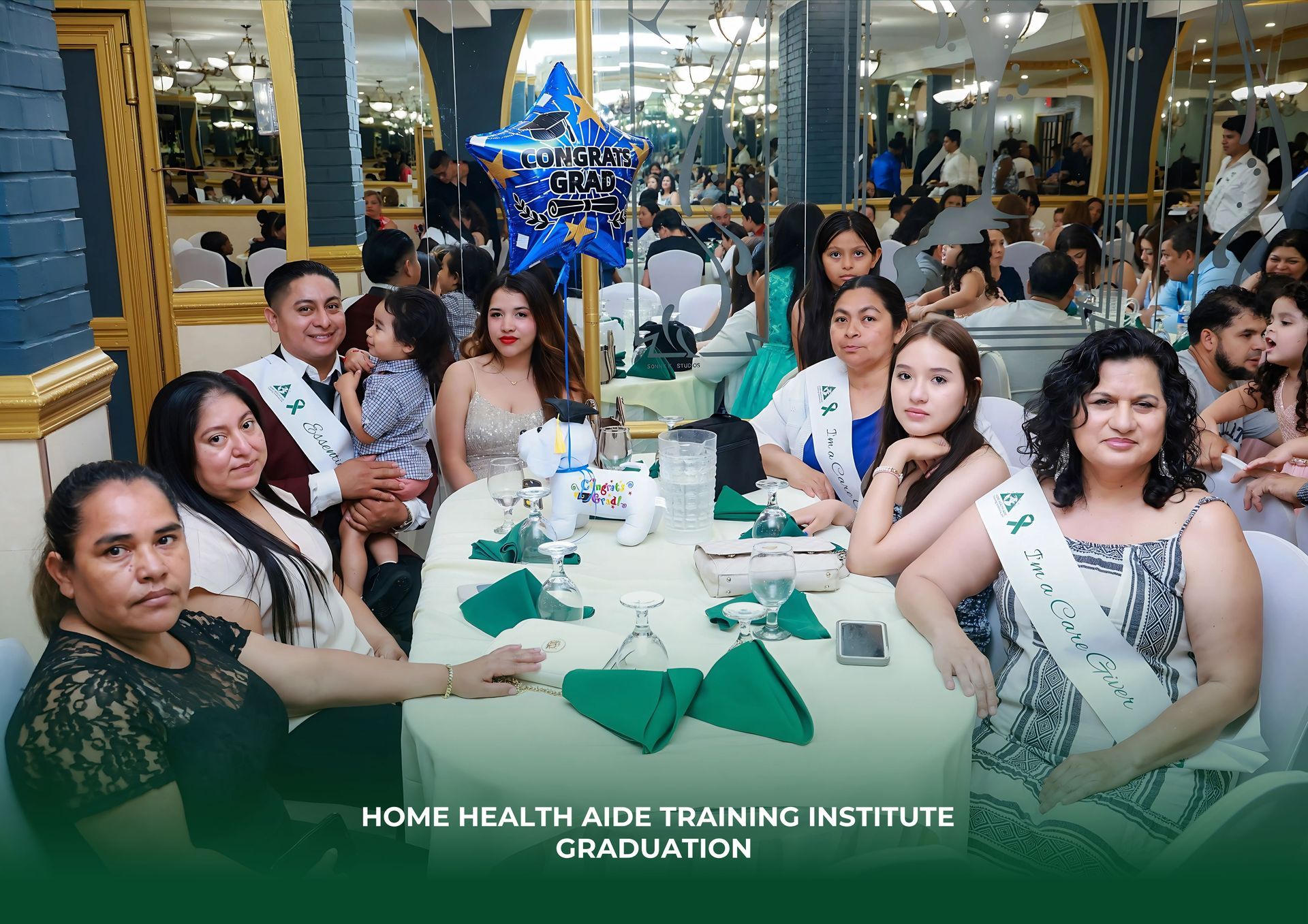 A group of people wearing graduation sashes sit at a table at a Home Health Aide Training Institute graduation event.