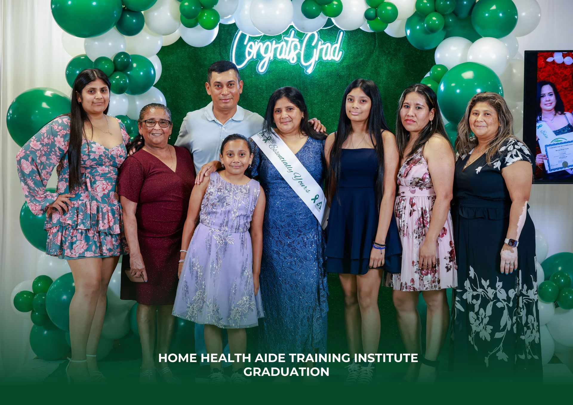 A group of nine people smiling in front of a green balloon wall with a 
