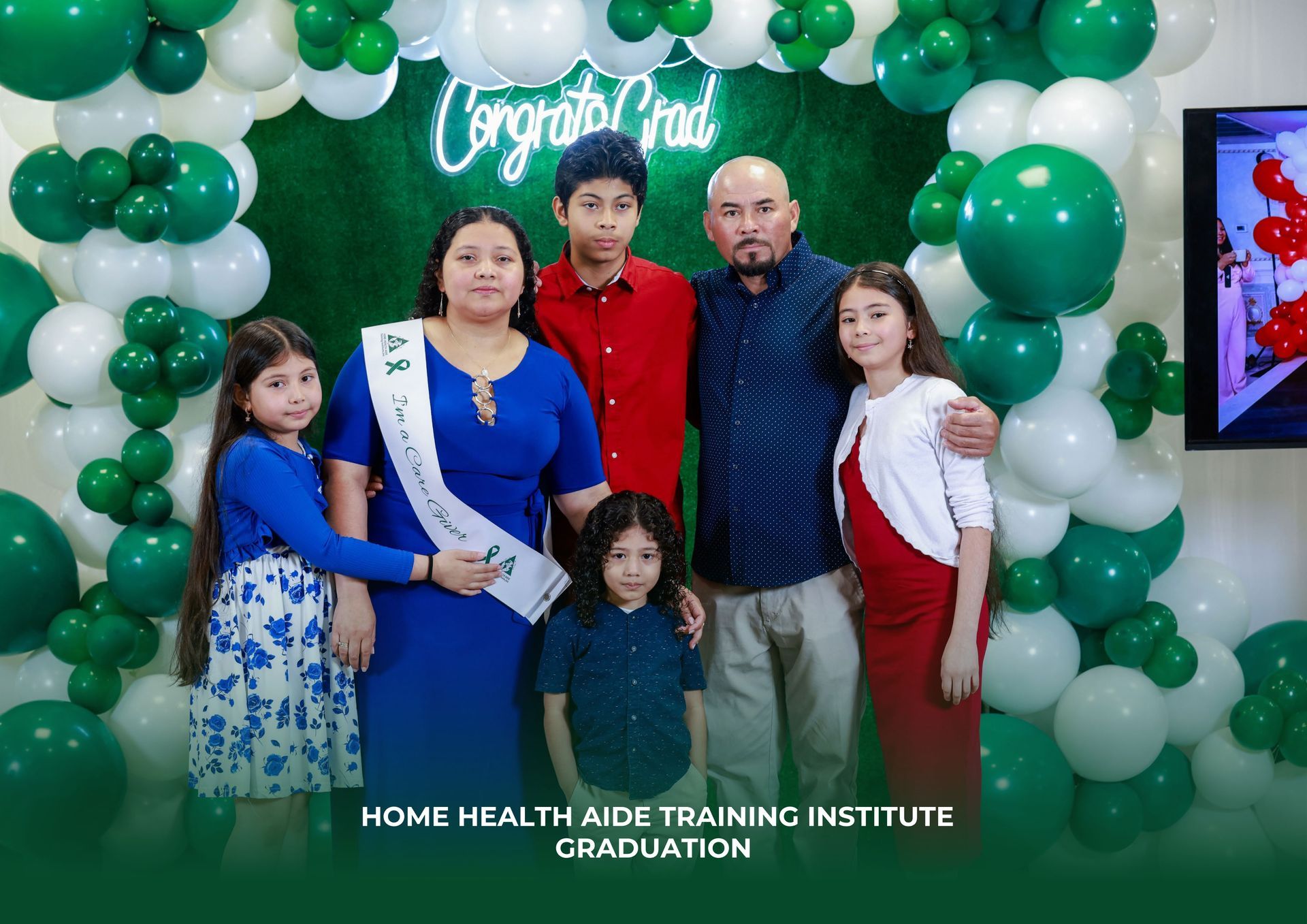 A family stands in front of a green and white balloon arch with a 