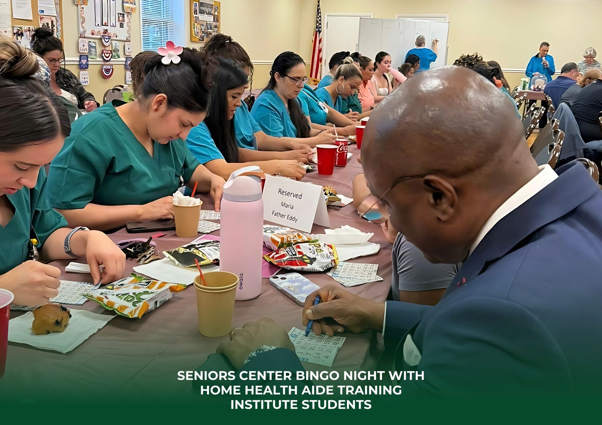 Students in green scrubs and others participate in a Bingo night at a seniors' center, sitting at tables with snacks.