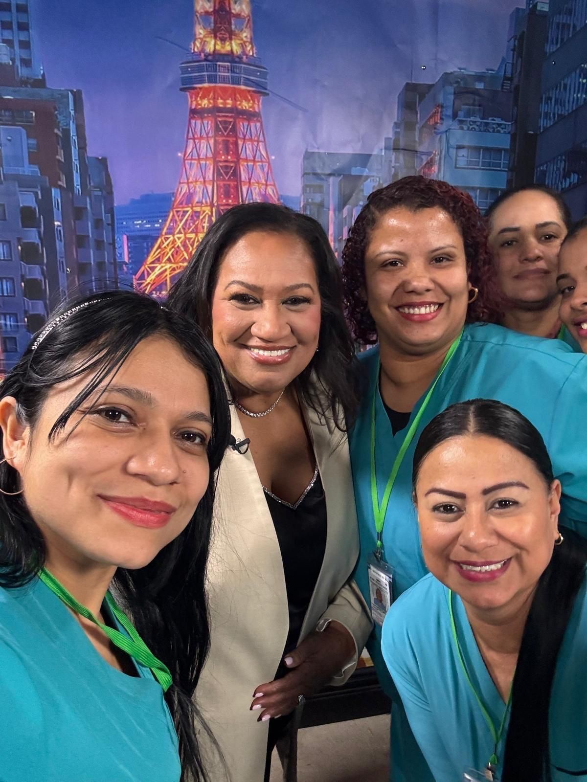 Five people smile together for a photo in front of a backdrop featuring a cityscape with a glowing tower.