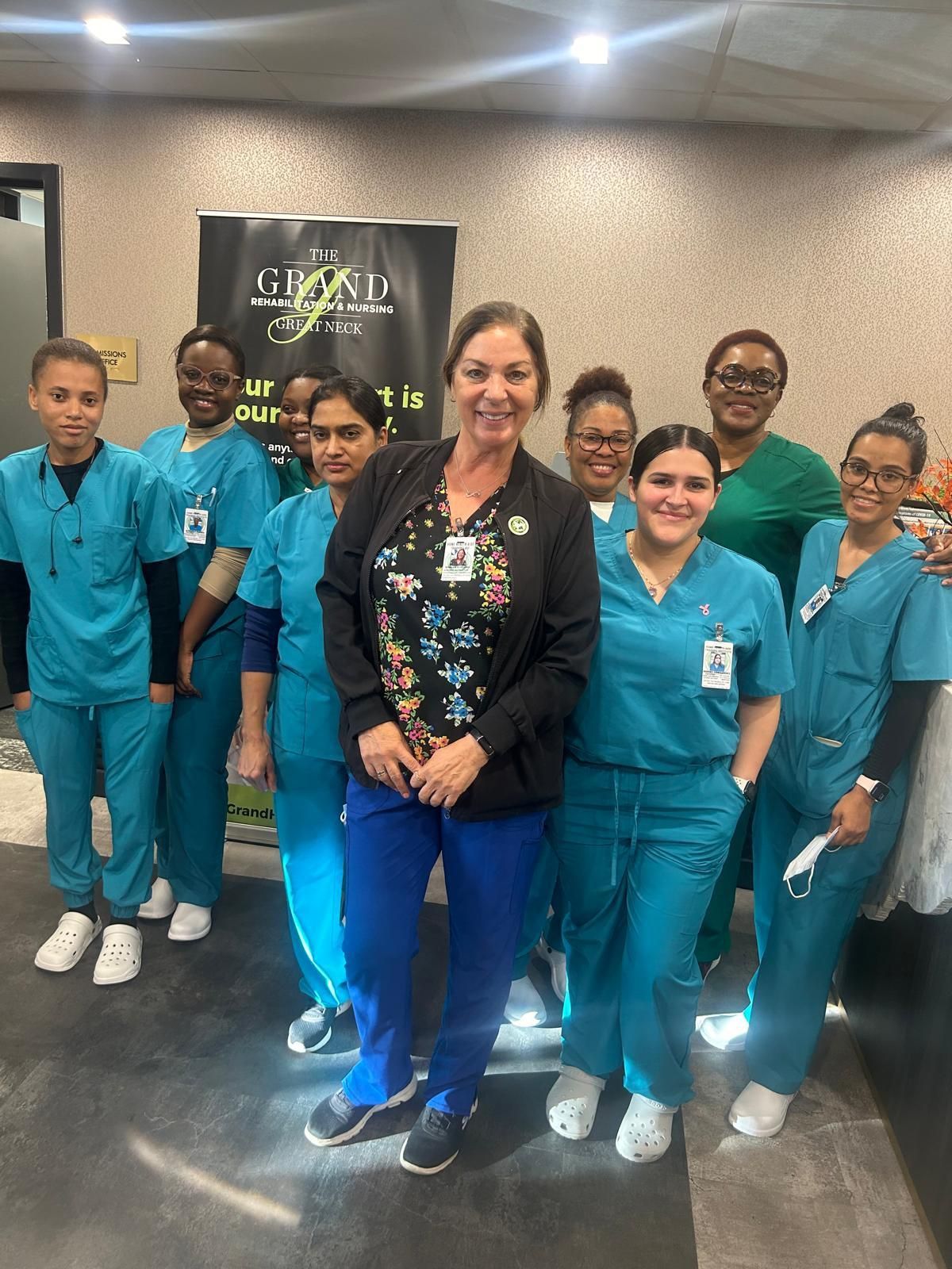 A group of staff in teal and blue medical scrubs smiling at the camera in a professional office setting.