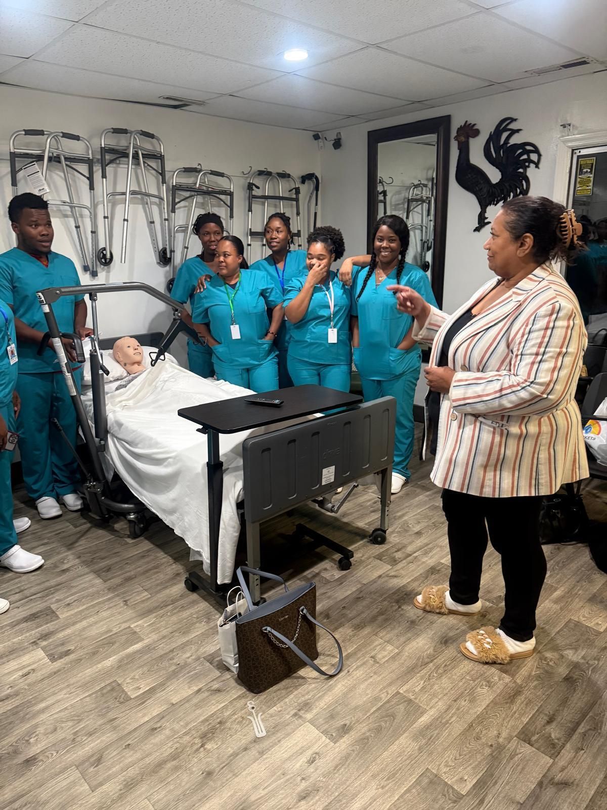 An instructor guides a group of nursing students in scrubs as they practice using a patient lift with a mannequin.