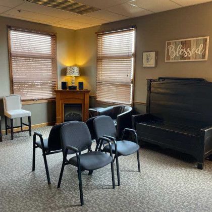 A waiting room with chairs, a bench, and two windows with blinds