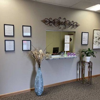 Reception area with desk, floral decor, framed documents, and a small plant.