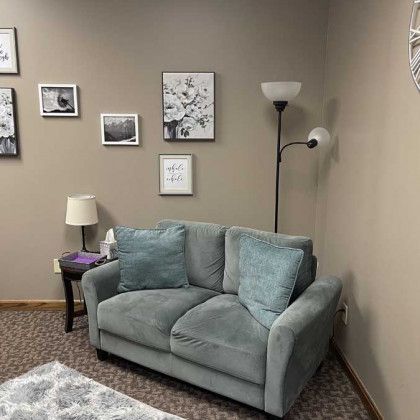 Cozy therapy room: blue loveseat, framed art, floor lamp, small table with lamp.