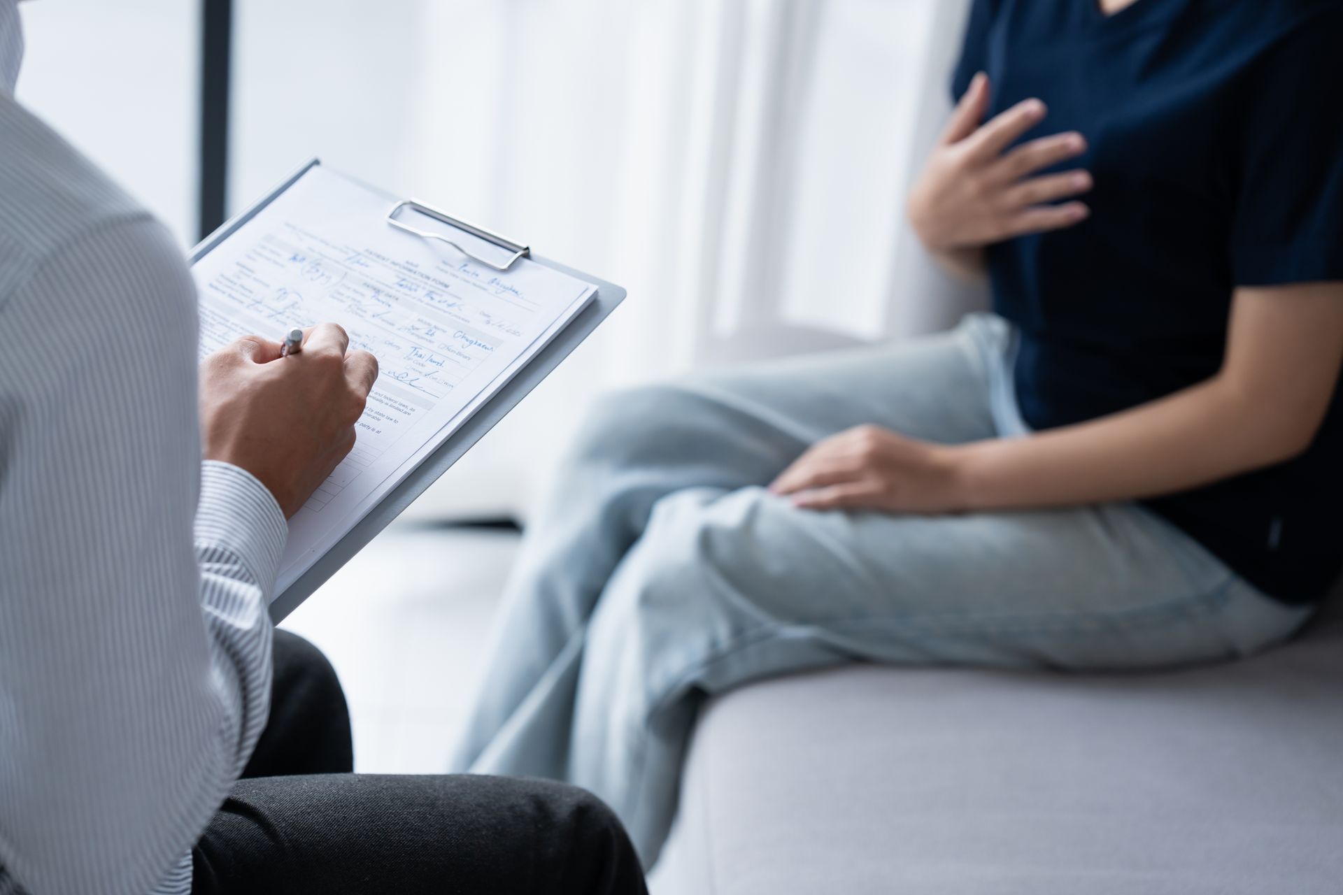 Therapist taking notes during session with patient, who is sitting and holding their chest.