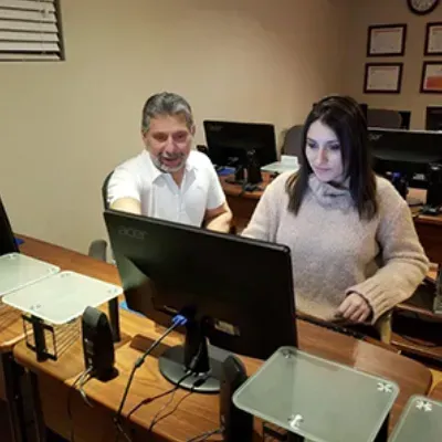 Two people seated at computers in an office, focused on their screens.