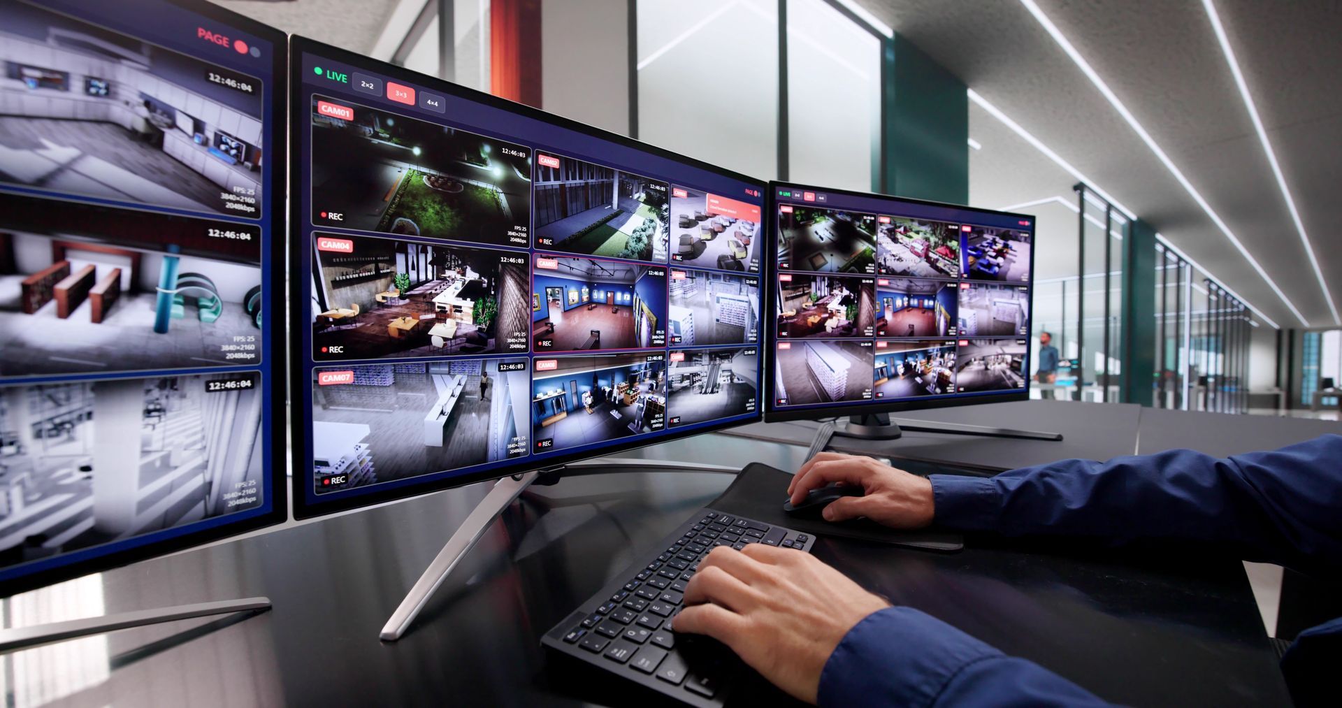 Operator monitoring multiple security camera feeds on several widescreen monitors at a control desk