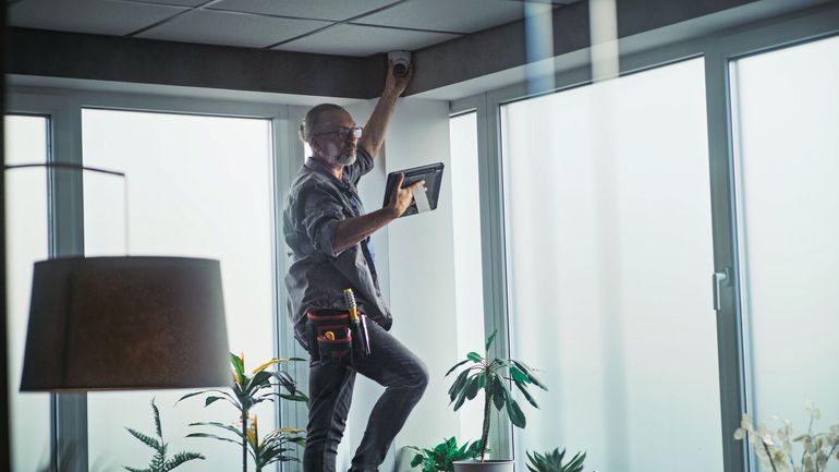 Worker installing a ceiling light in a bright room with large windows