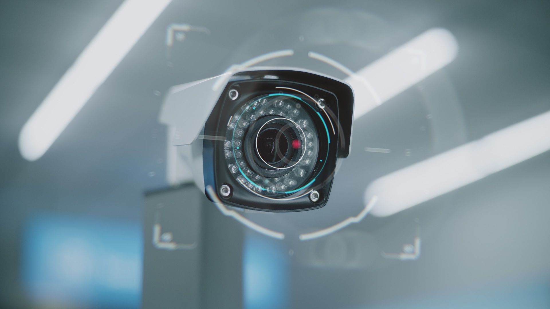 Close-up of a white security camera with a black lens, mounted indoors against a blurred modern background