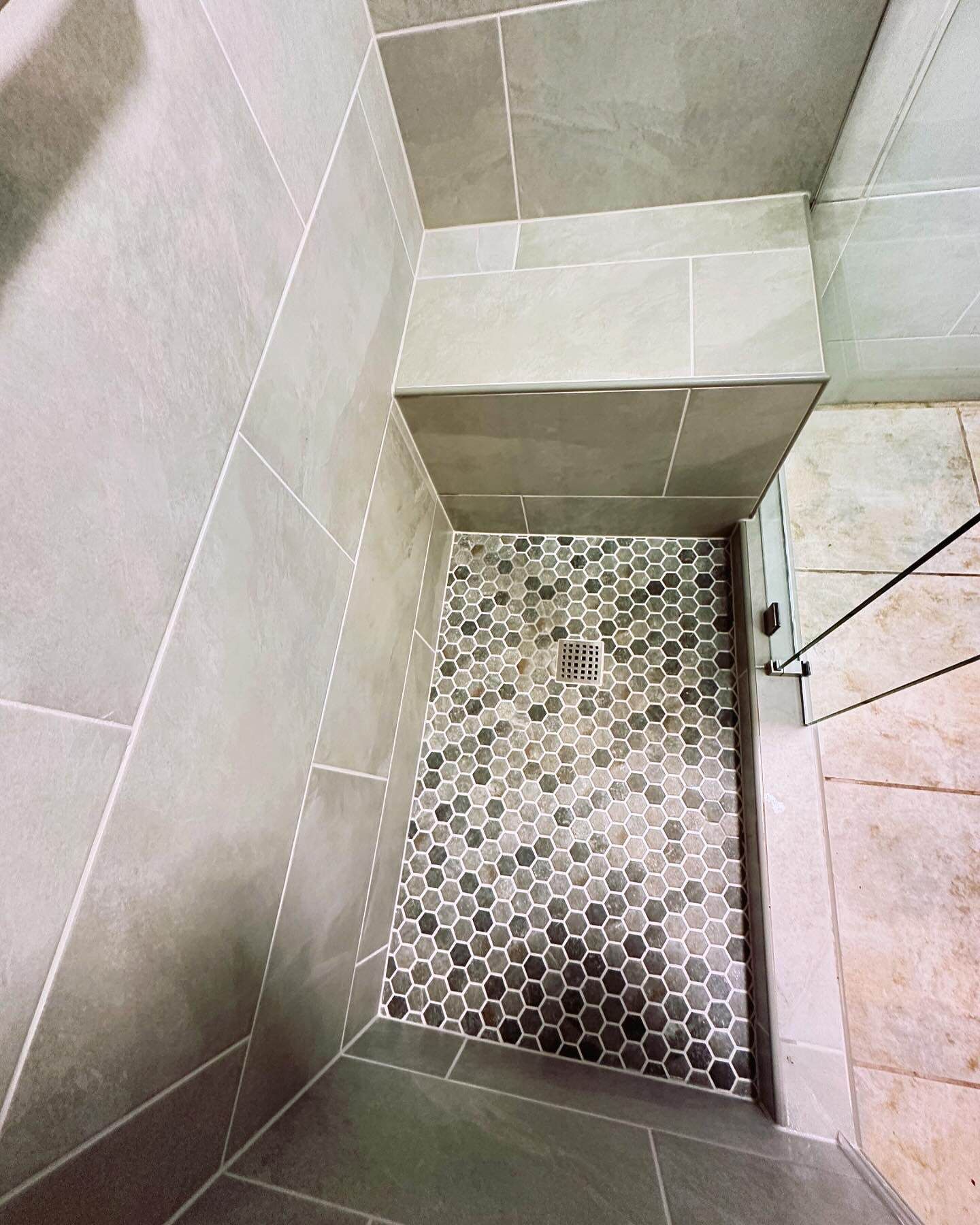 Small tiled shower stall with a mosaic floor and built-in bench, viewed from above.