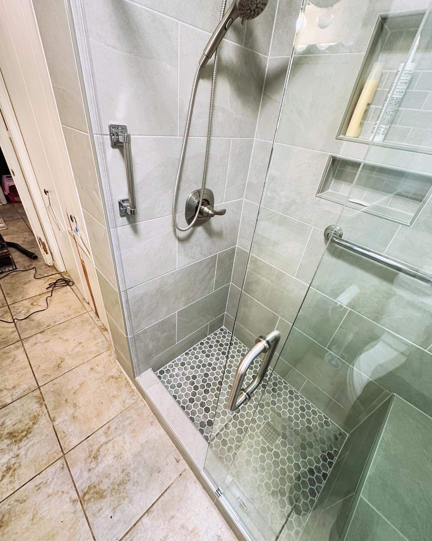 Glass walk-in shower with pebble floor, wall grab bar, and tiled walls