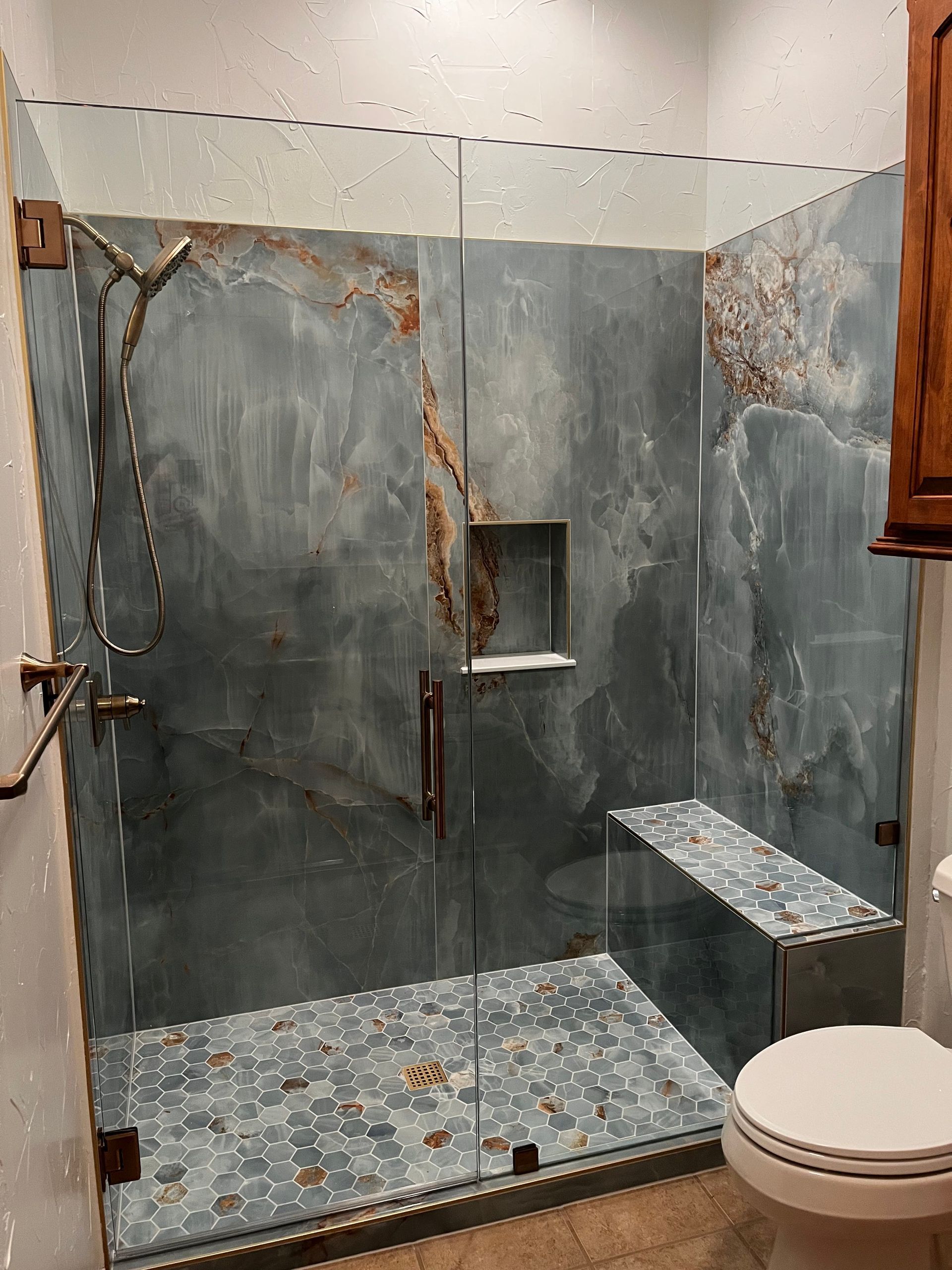 Small tiled bathroom with a walk-in shower, gray stone walls, glass doors, and a toilet in the foreground