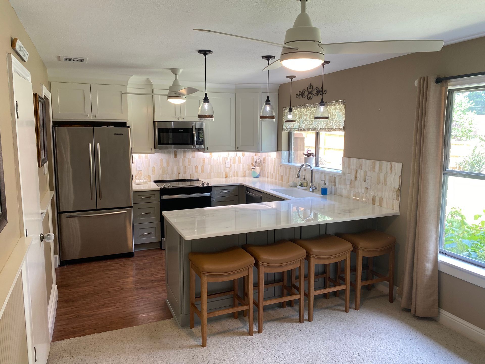 Bright kitchen with stainless steel appliances, gray island, bar stools, and large window.