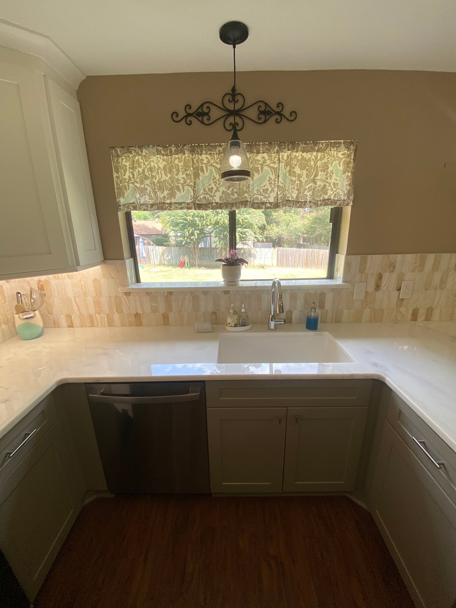 Small kitchen with white counters, dark cabinets, sink under a window, and a decorative pendant light.