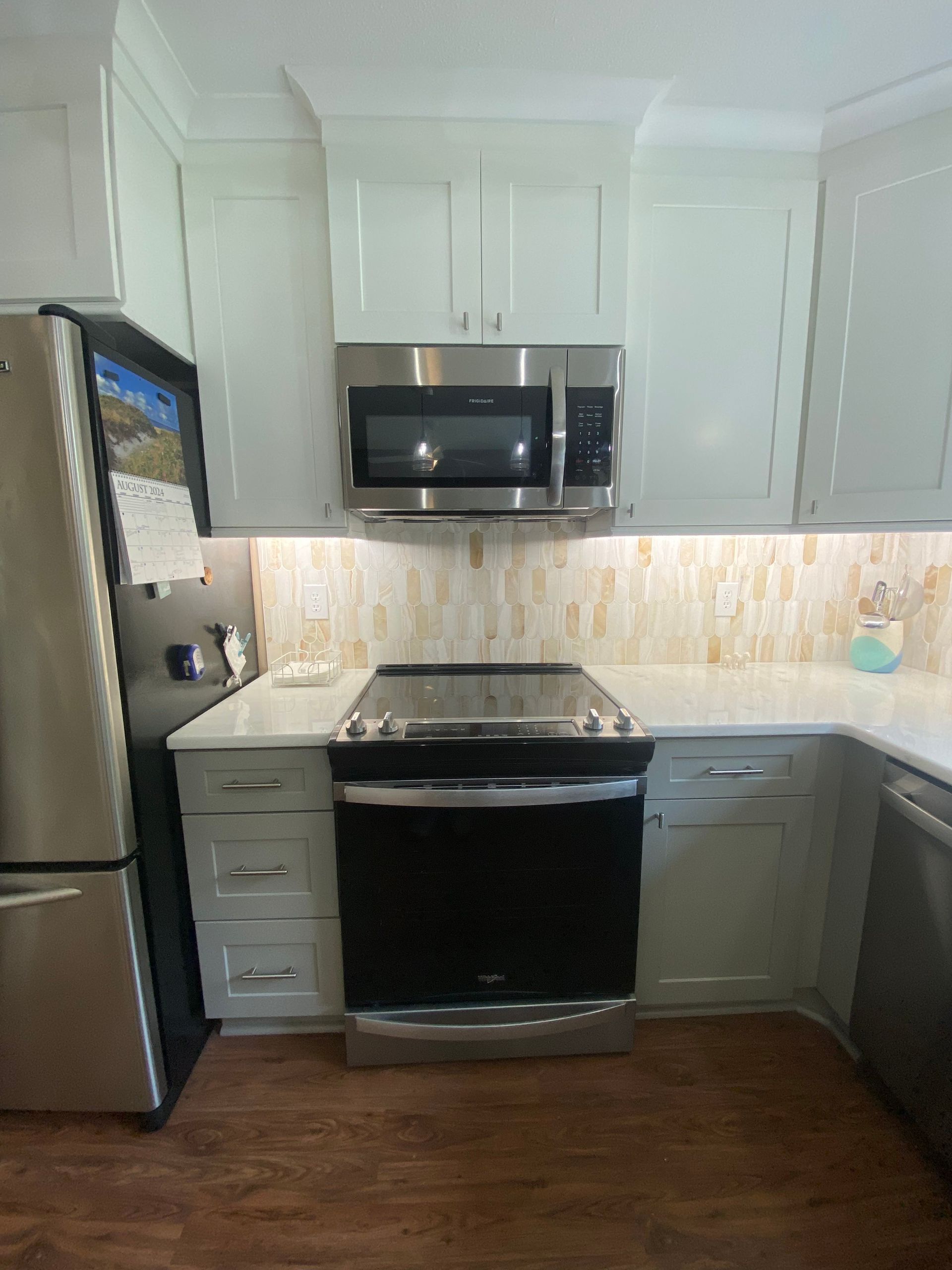 Small kitchen with stainless steel appliances, white cabinets, and dark wood flooring.