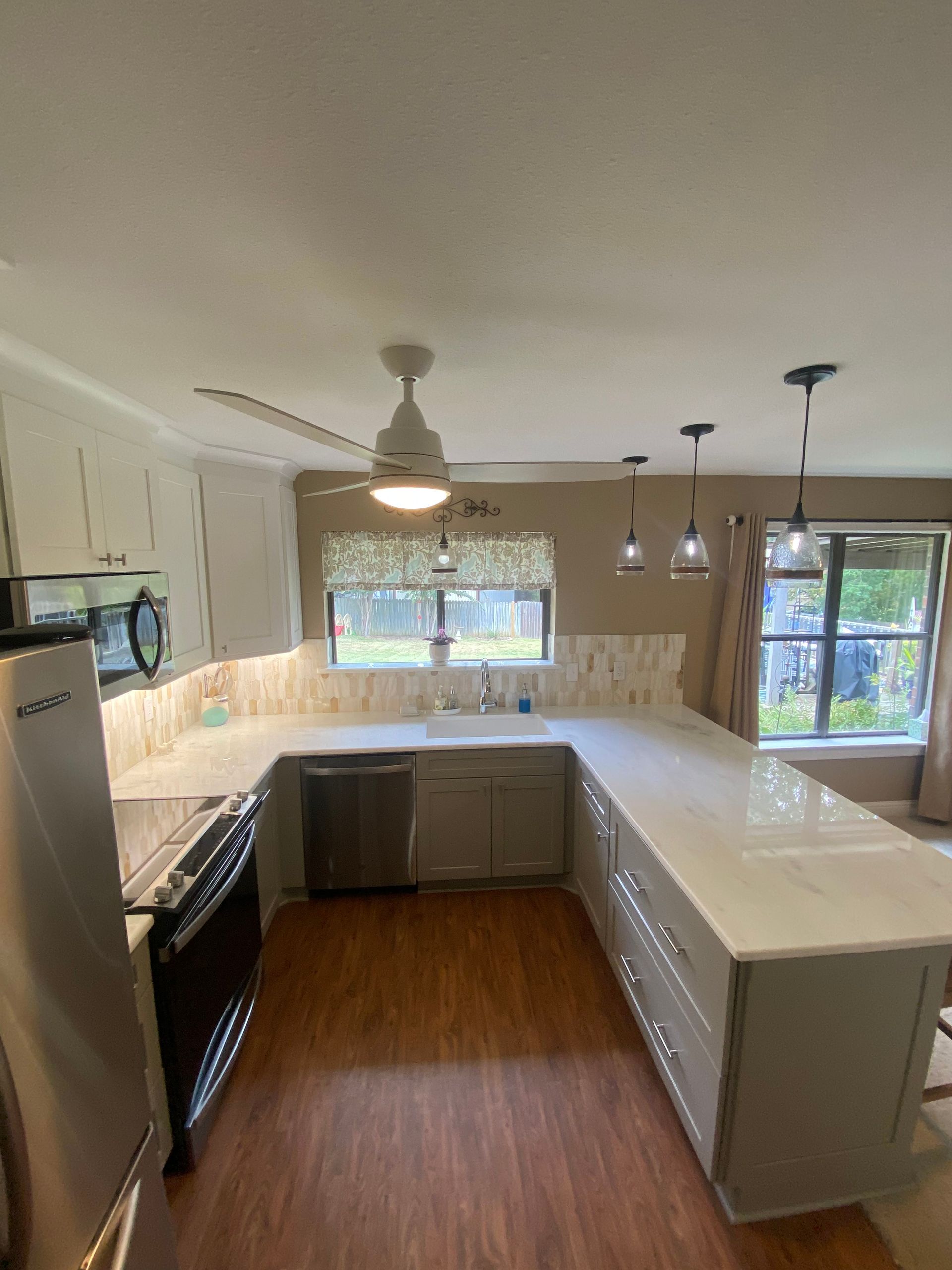 Bright kitchen with white countertops, gray cabinets, wood floors, and a window over the sink.