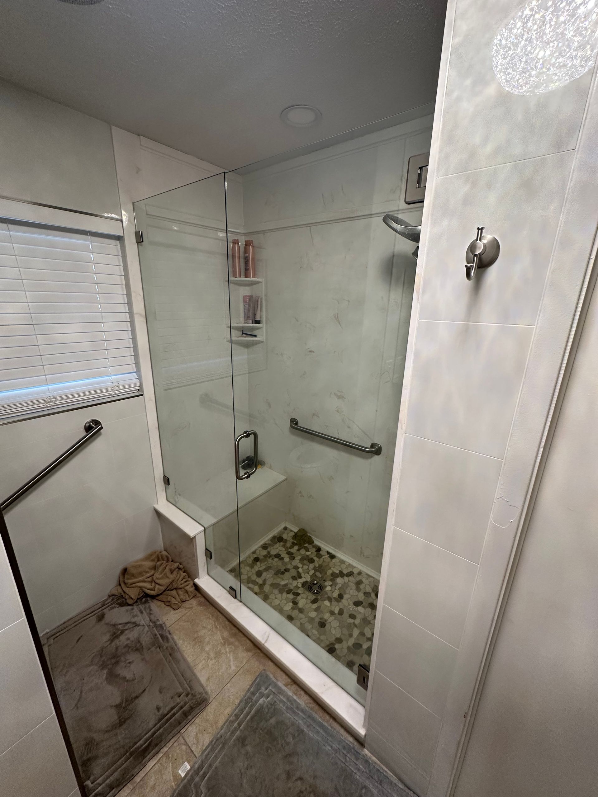 Empty tiled shower with glass partition, window, built-in shelves, and a bath mat on the floor.