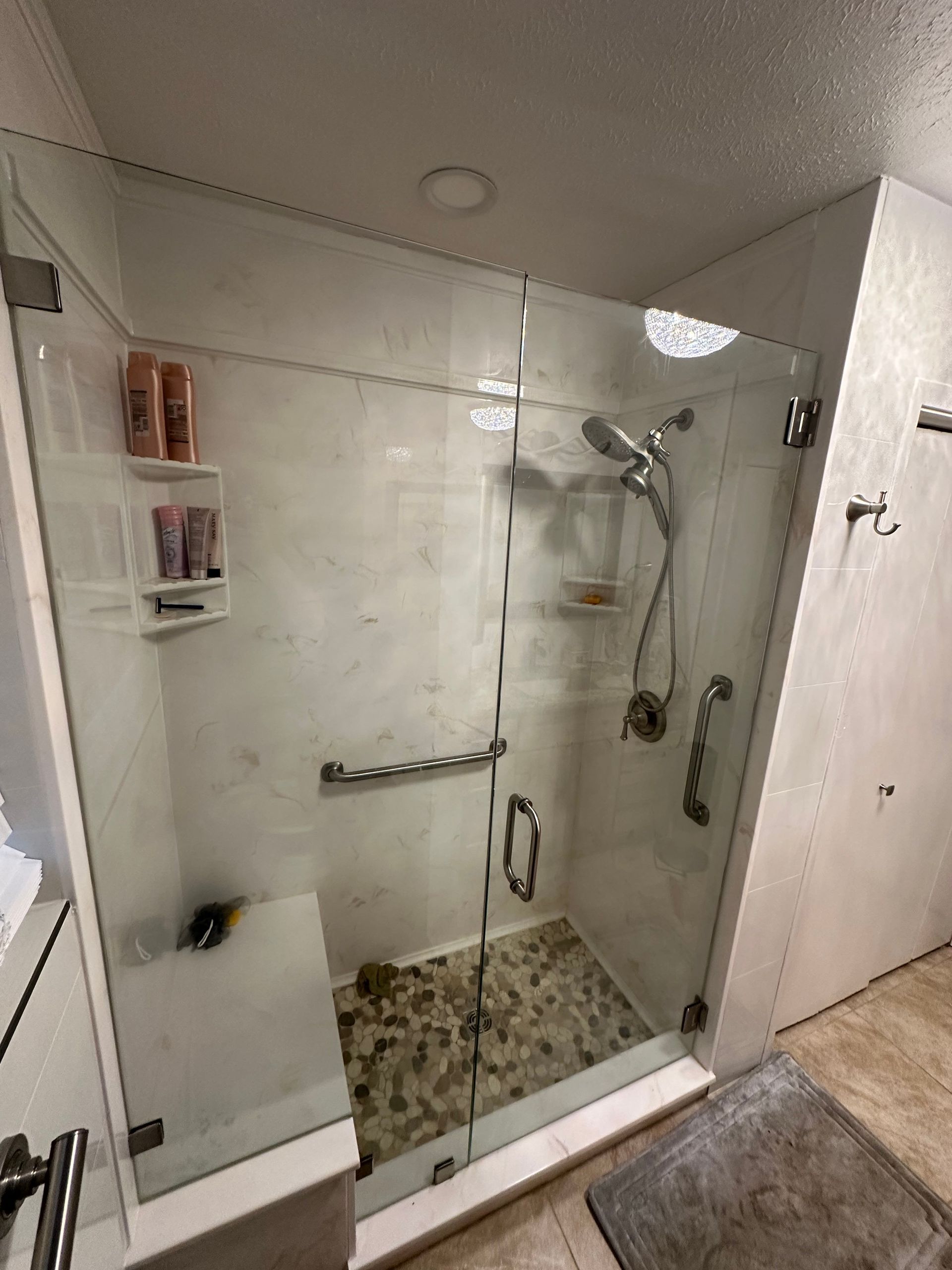 Glass shower stall with chrome fixtures, pebble floor, and wall shelf in a white bathroom