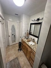 Narrow bathroom with vanity, mirror, towels, and a bathrobe hanging on the door.
