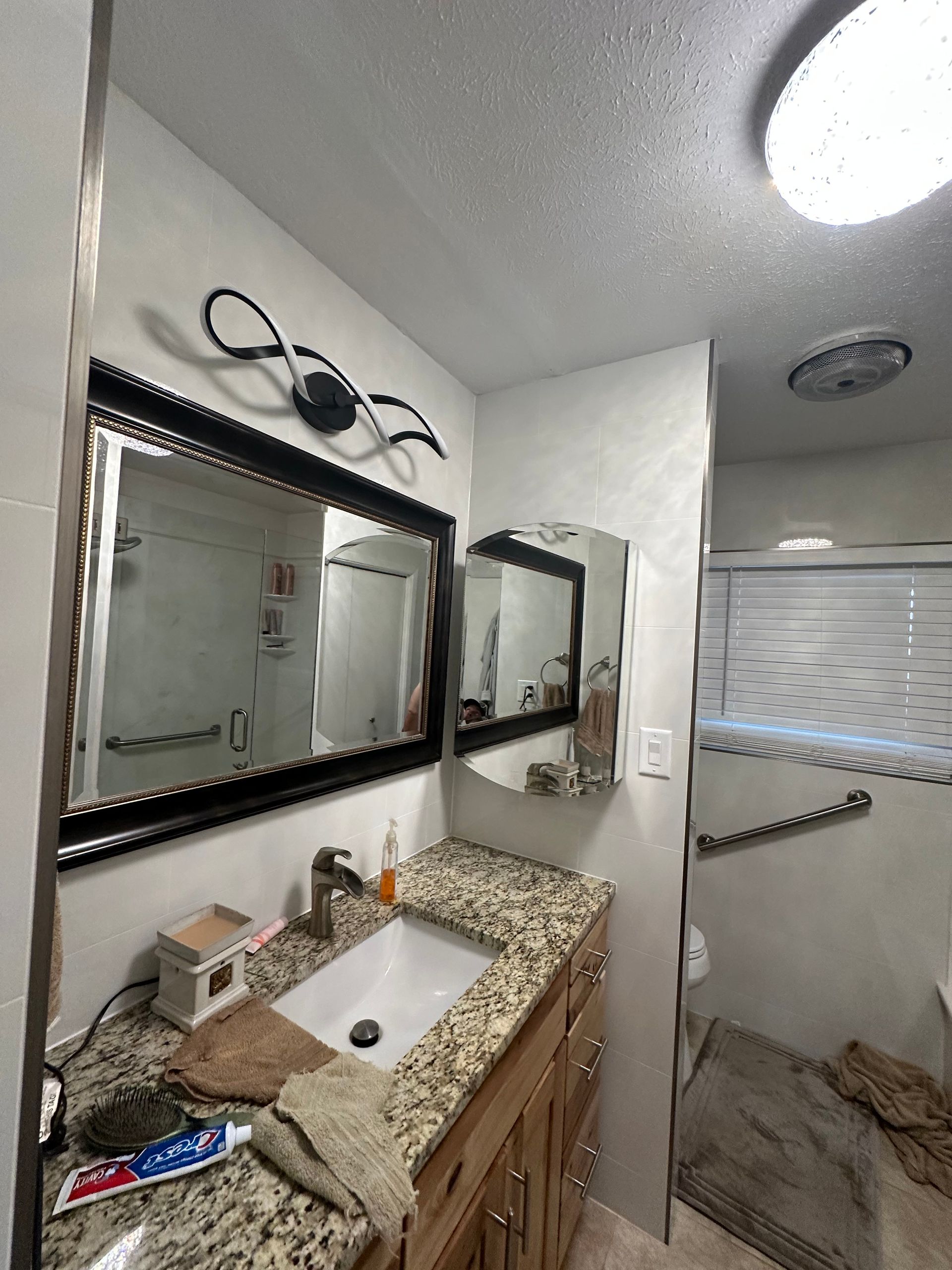 Bathroom vanity with granite countertop, mirrors, and tiled shower in the background