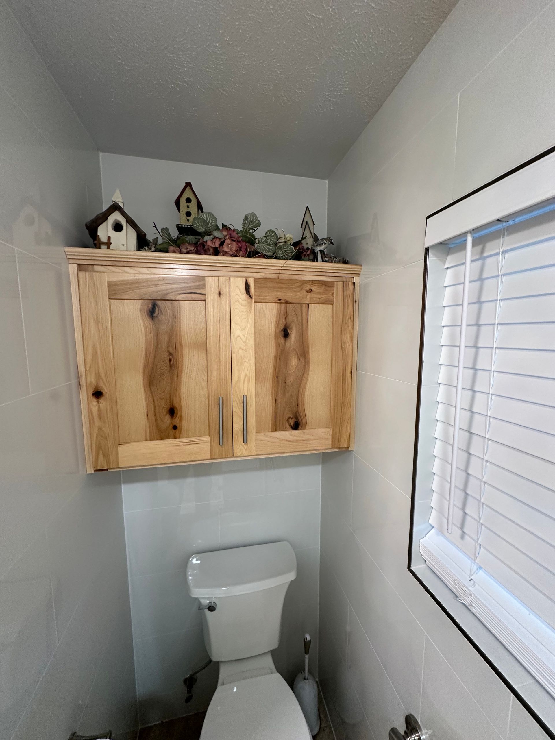 Small bathroom with white toilet, wooden wall cabinet, and window blinds above the toilet