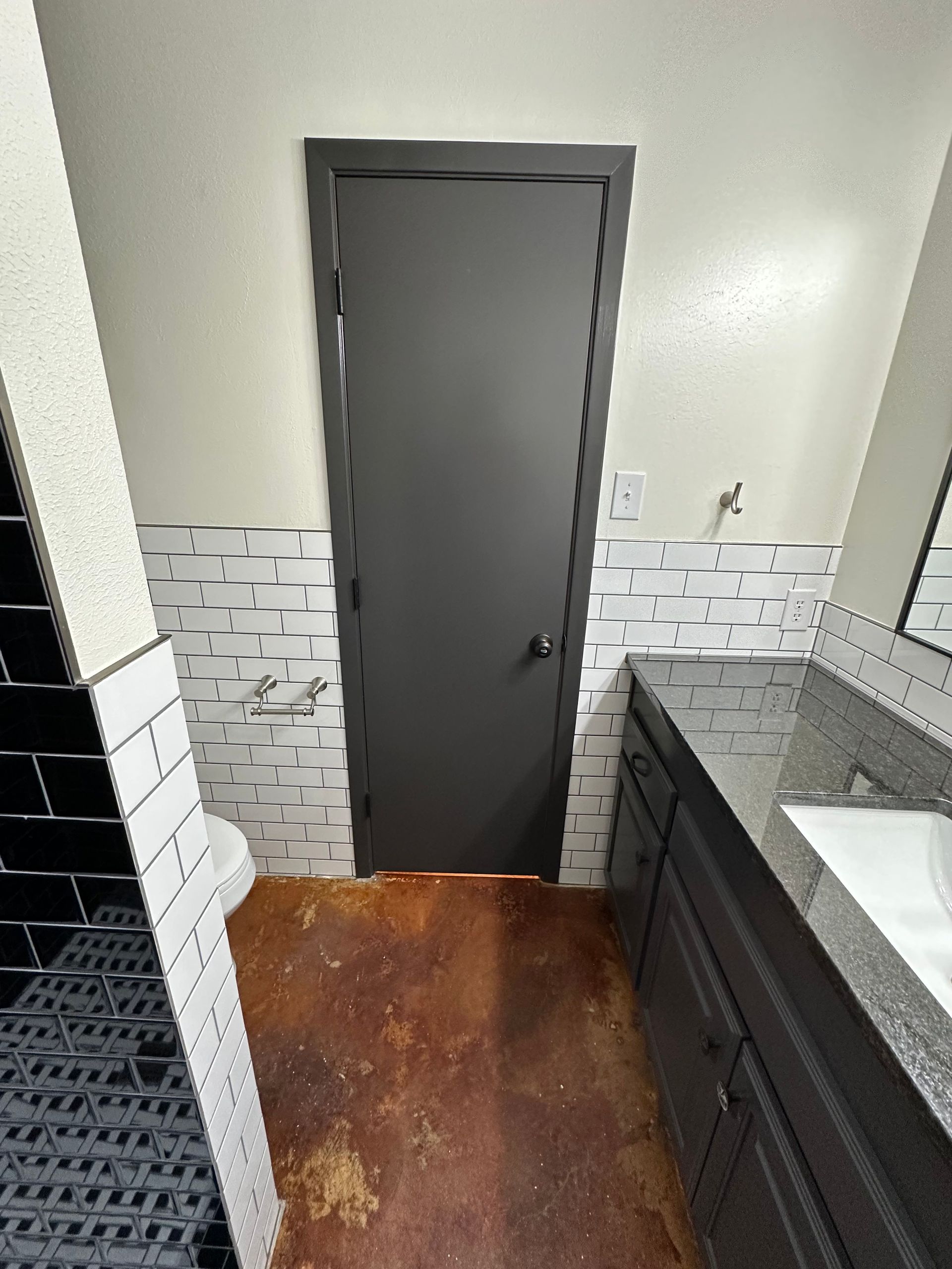 Small bathroom with dark gray door, white tiled walls, black vanity, and wooden floor.