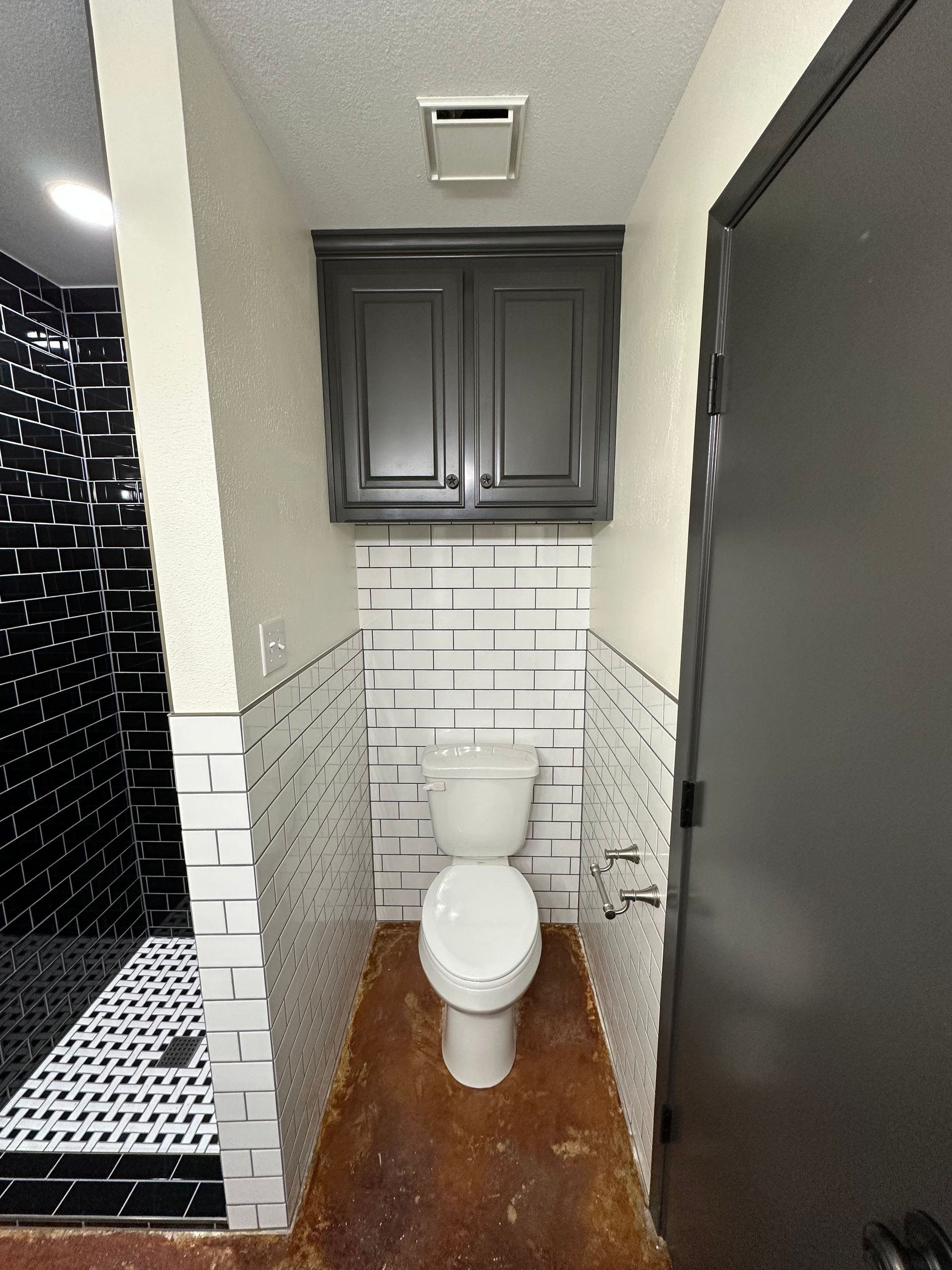 Small restroom with a toilet, white subway tile, dark cabinet above, and black-and-white shower tile beside it.